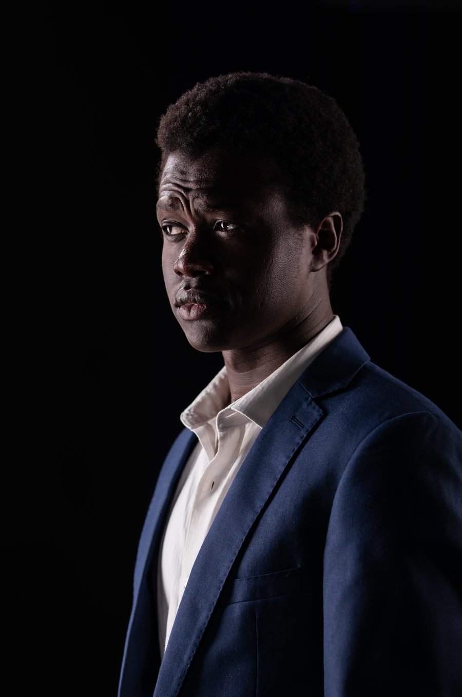 A studio headshot, three-quarter pose, in a navy blazer