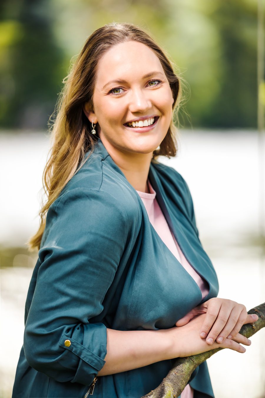 A woman in a teal jacket, over-the-shoulder pose, looking back at the camera