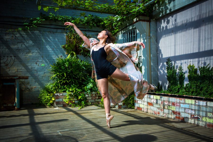 A ballet dancer mid-arabesque in a weathered industrial space