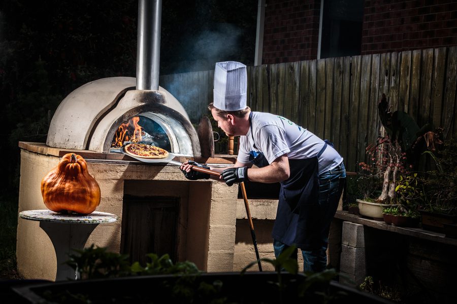 A man at a pizza oven at night, lit by the fire, dramatic and strong