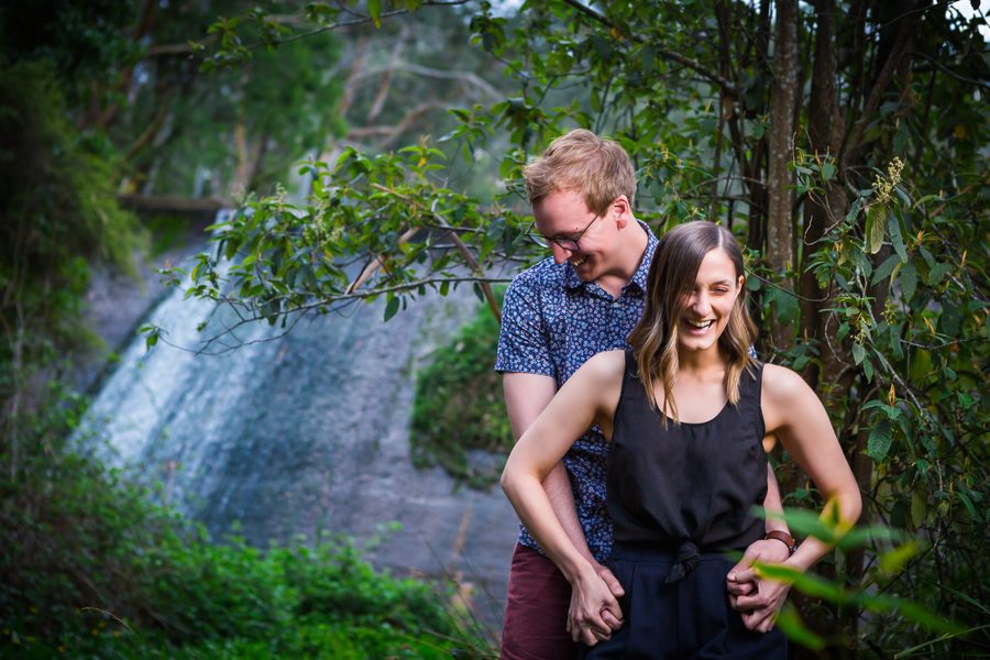 A couple laughing together beside a creek surrounded by lush green