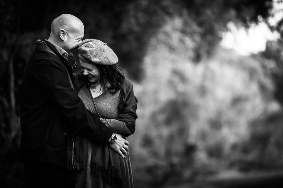 A couple portrait beside moss-covered branches in warm natural light
