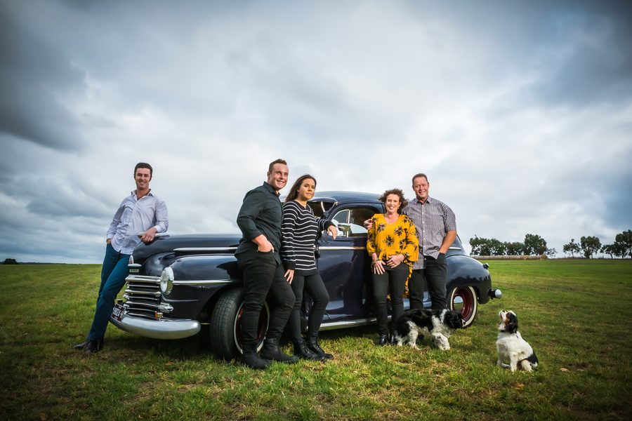 A family with two dogs beside a vintage car in an open field