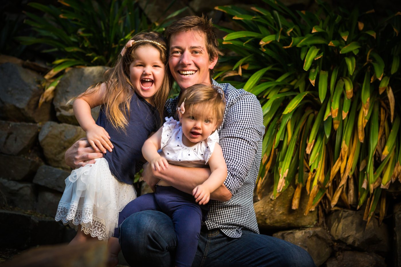 A father, mother and two daughters together outdoors in a close pyramid composition