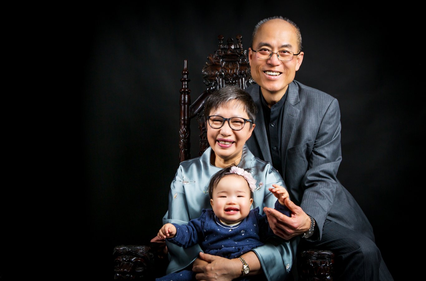 Three-person family on ornate chair, studio, black background