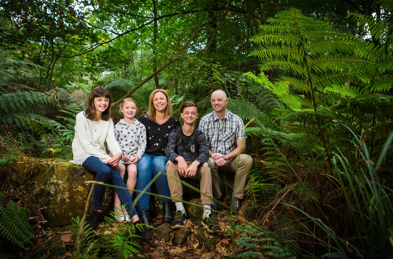 Family of five arranged on log in lush fern forest
