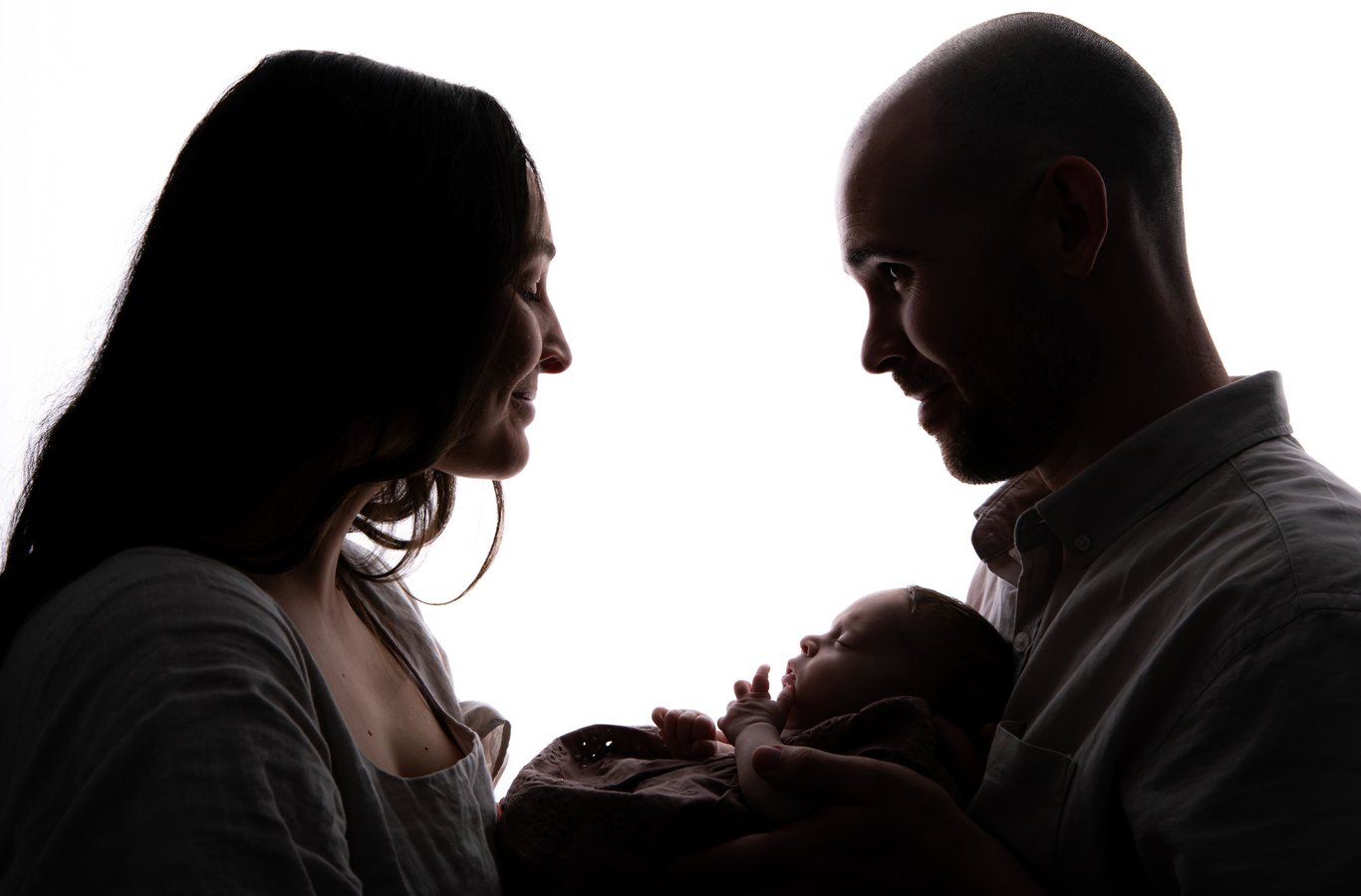 Silhouetted couple with infant backlit against white