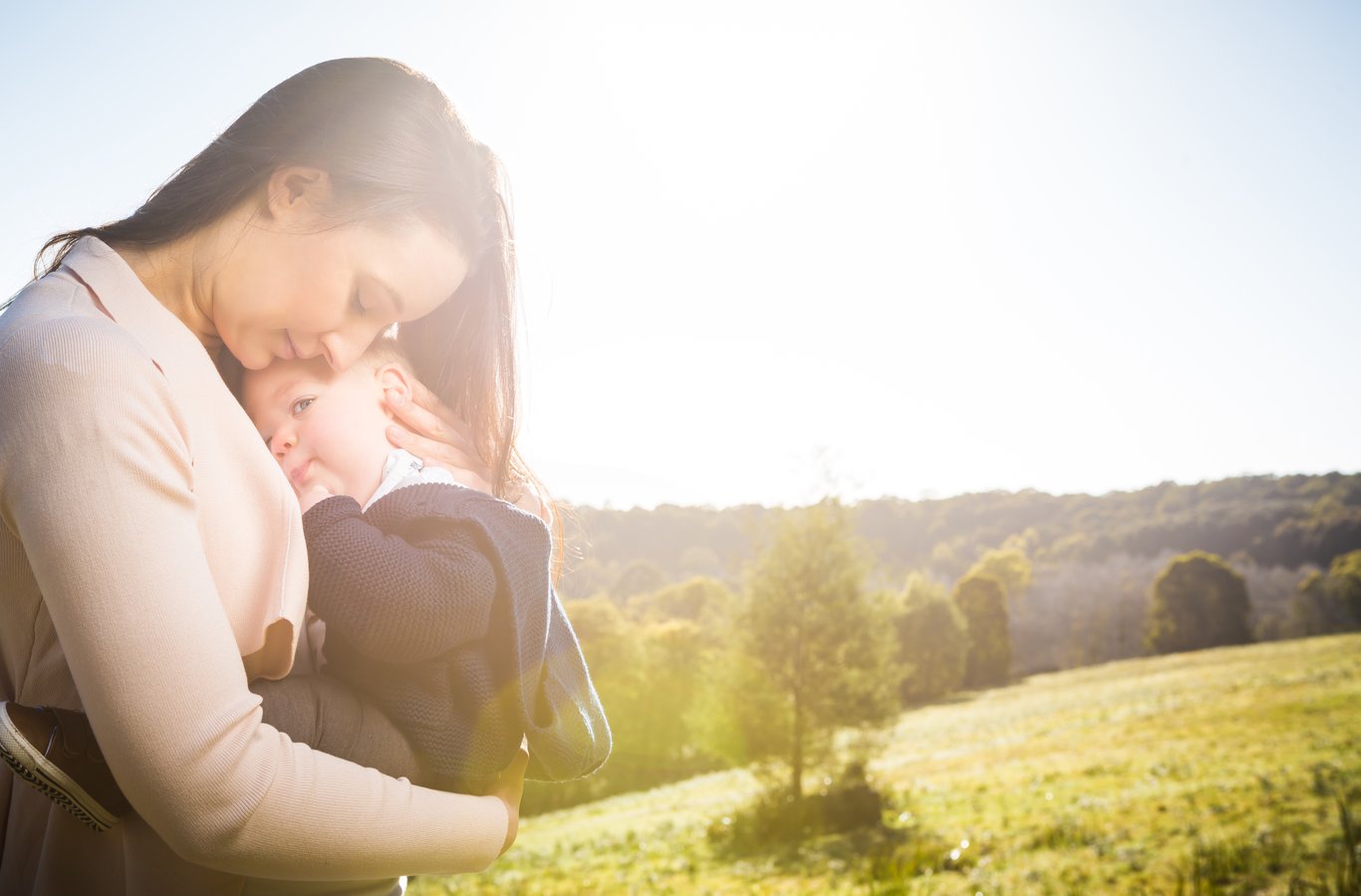 Mother holding toddler, both backlit by golden-hour light